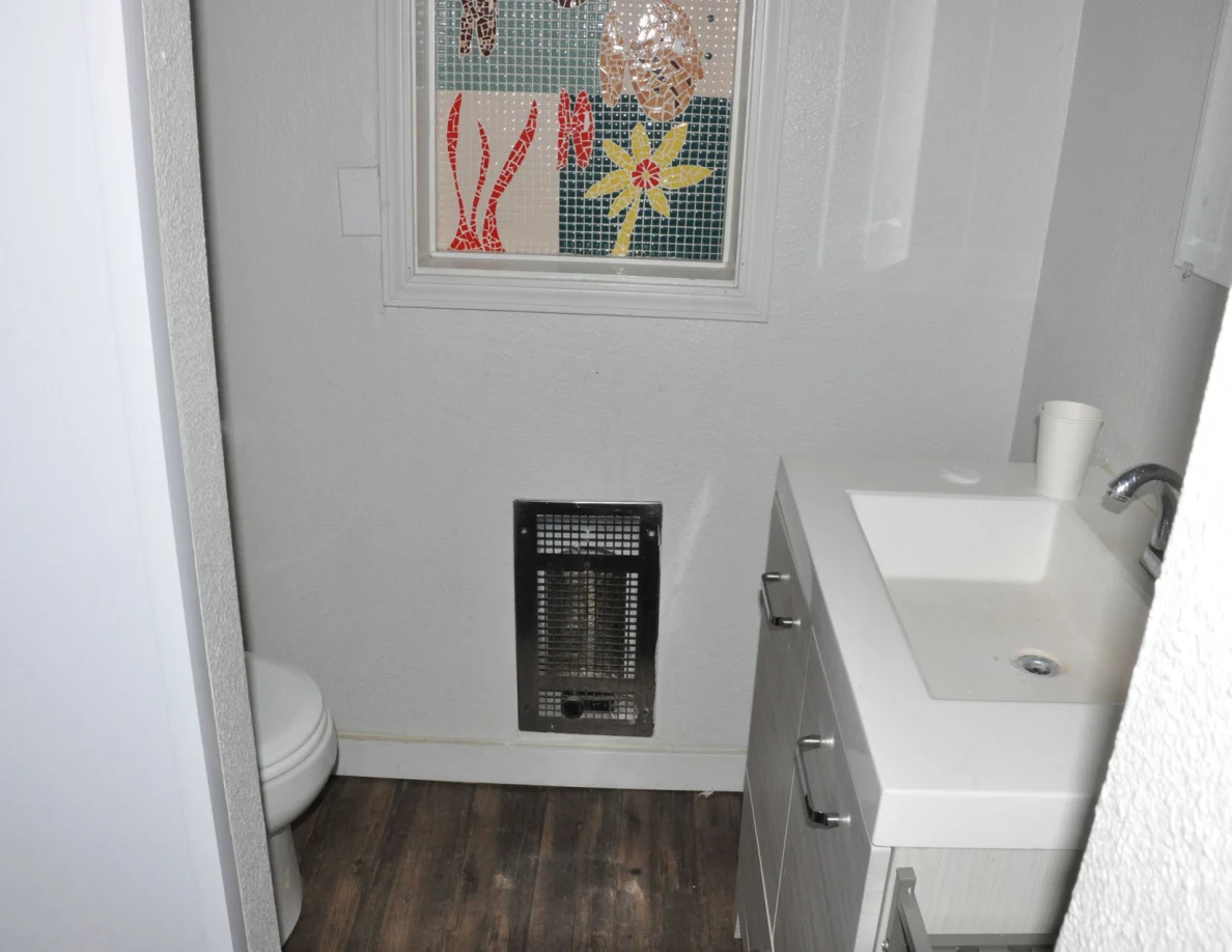 Bathroom vanity and partial toilet below a decorative panel, with a wall heater near the floor.