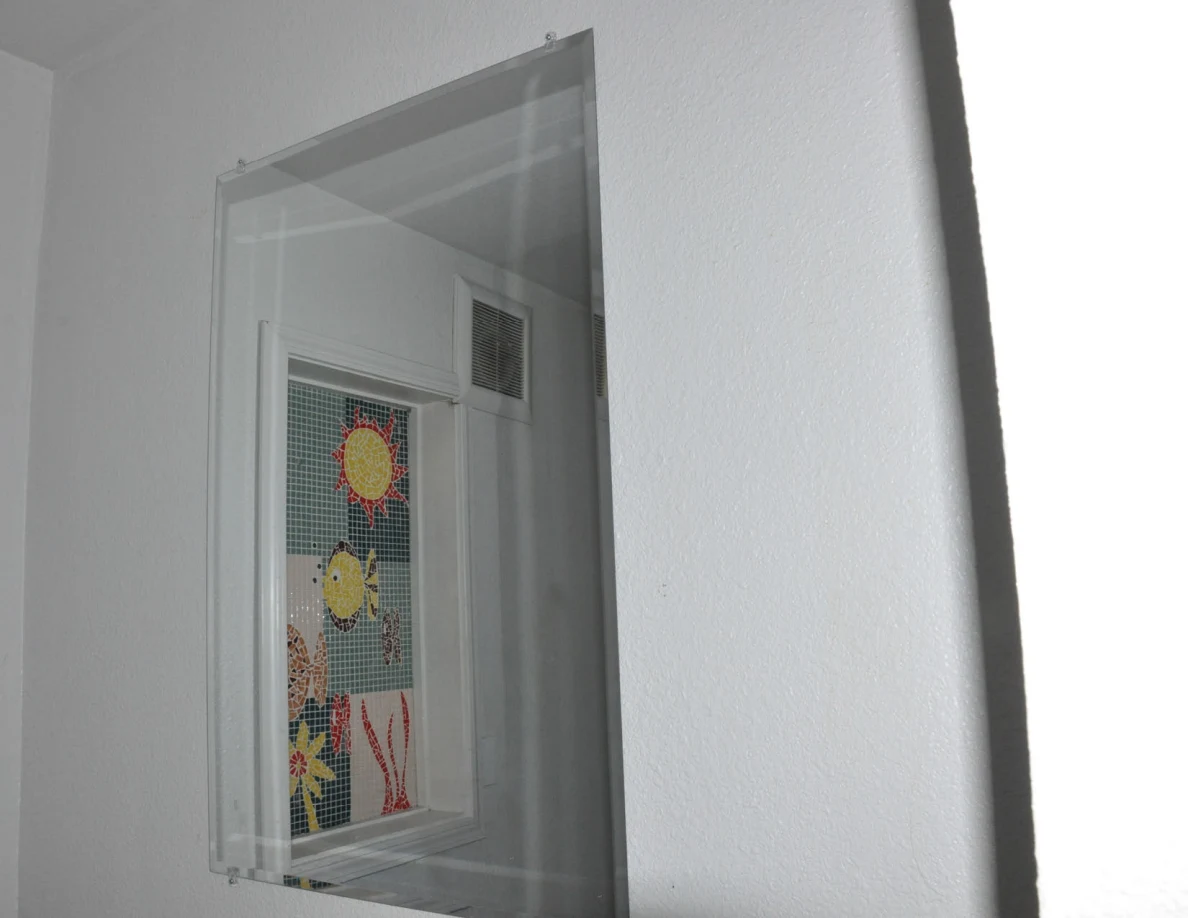 Wall mirror reflecting a colorful decorative bathroom window panel.