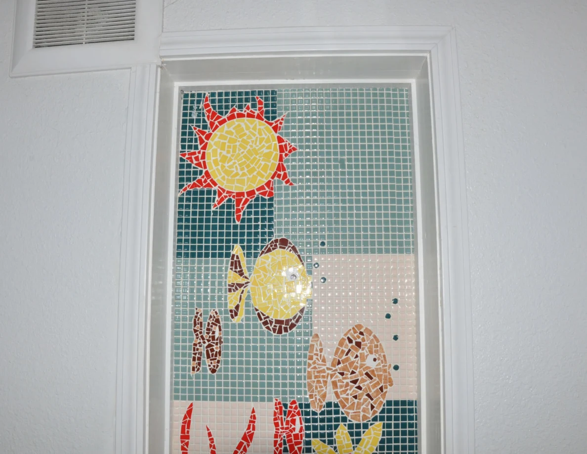 Close view of a colorful sun-and-fish mosaic-style window panel.