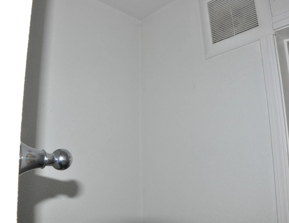 Plain white bathroom corner with a ventilation grille near the ceiling.