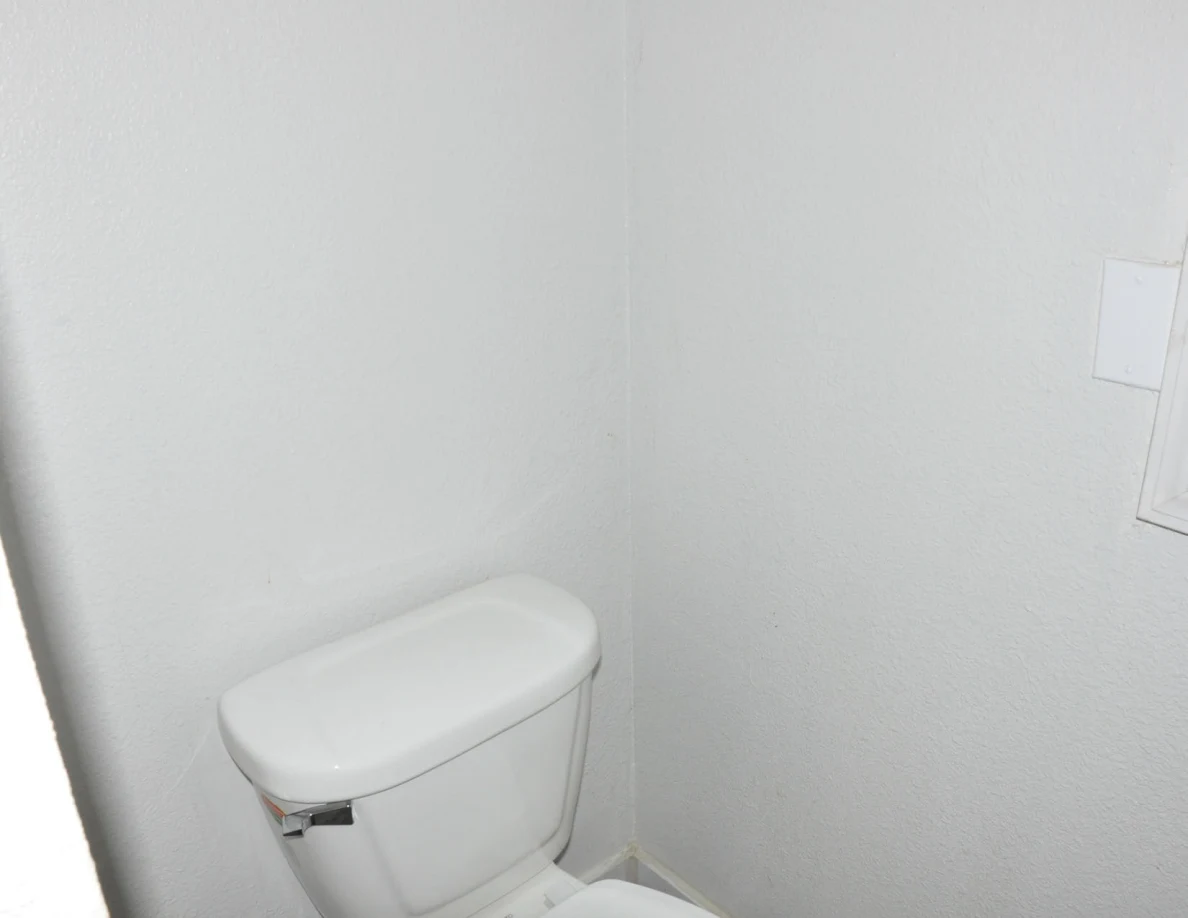 White toilet tank against a white bathroom wall.