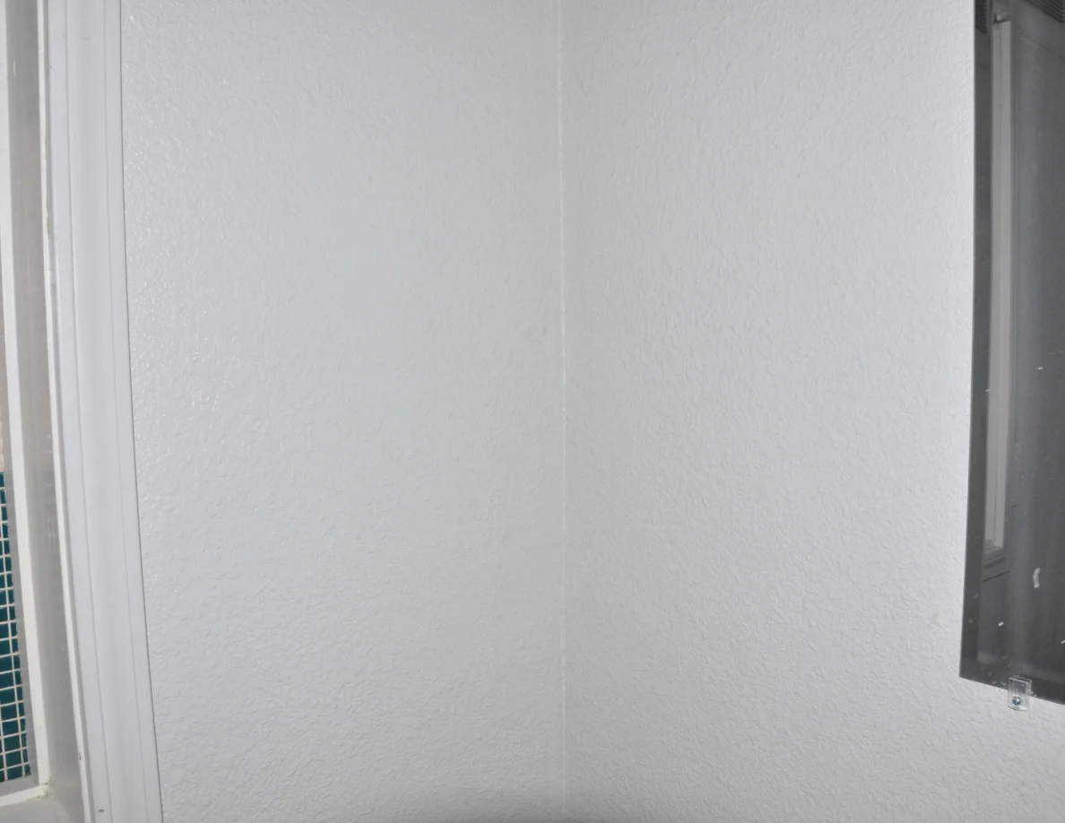 Plain white bathroom wall between window trim and mirror edge.
