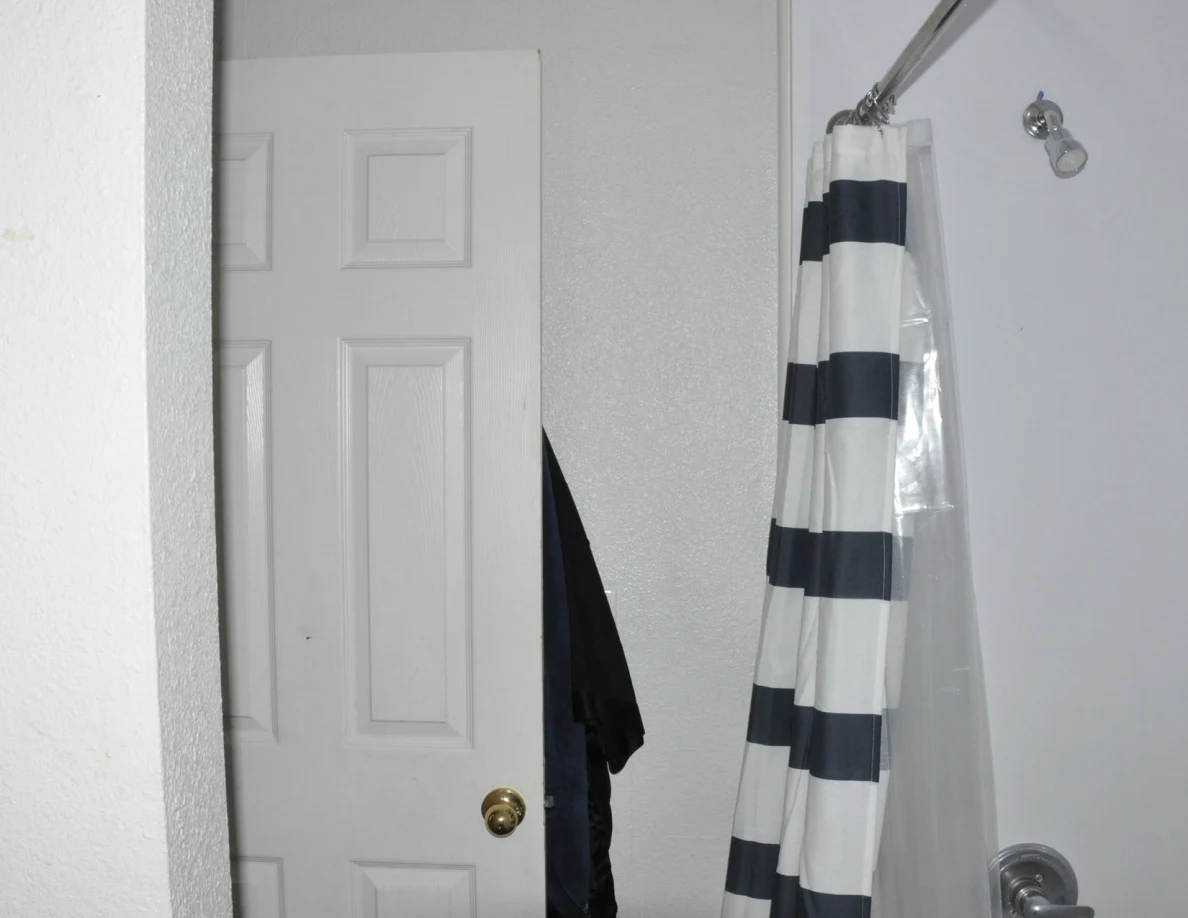 Upper bathroom view with shower head, striped curtain and white door.