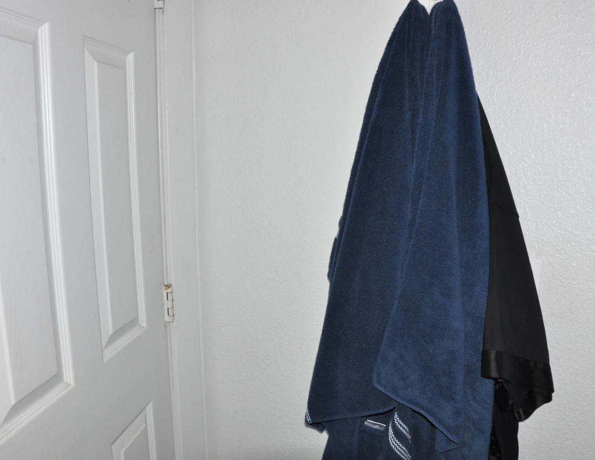Blue towel and dark fabric hanging from a hook beside a white door.
