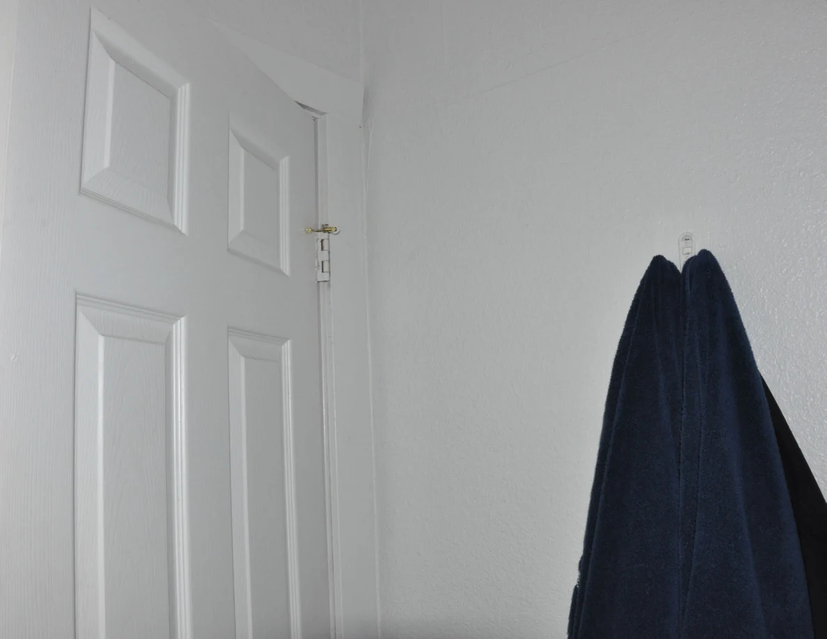 Upper corner of a white bathroom door beside hanging blue towels.