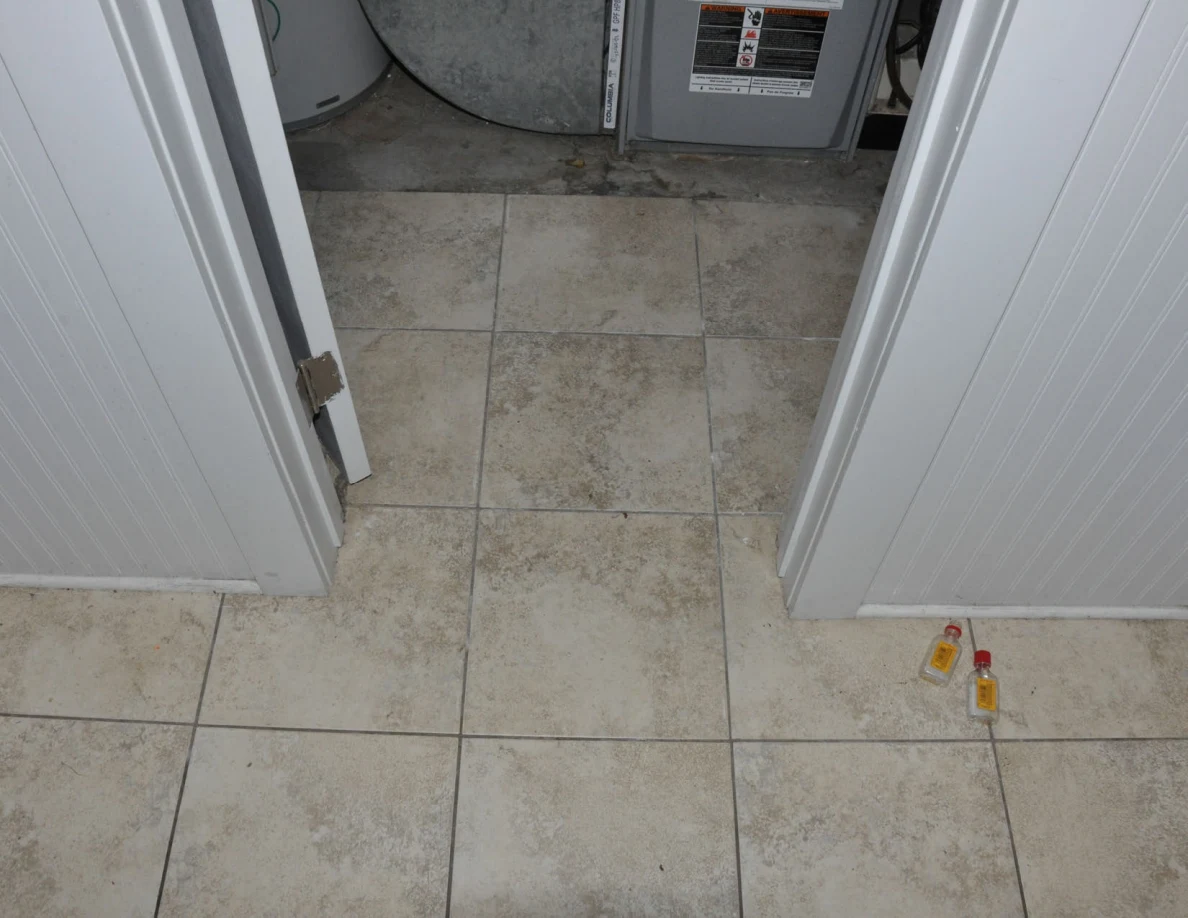 Utility-room threshold with furnace equipment beyond and two small bottles on the hallway floor.