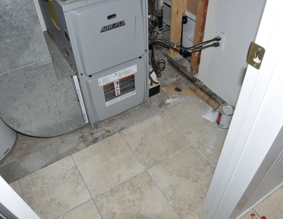 Furnace base and exposed cables beside a utility-room floor with a small paint can.
