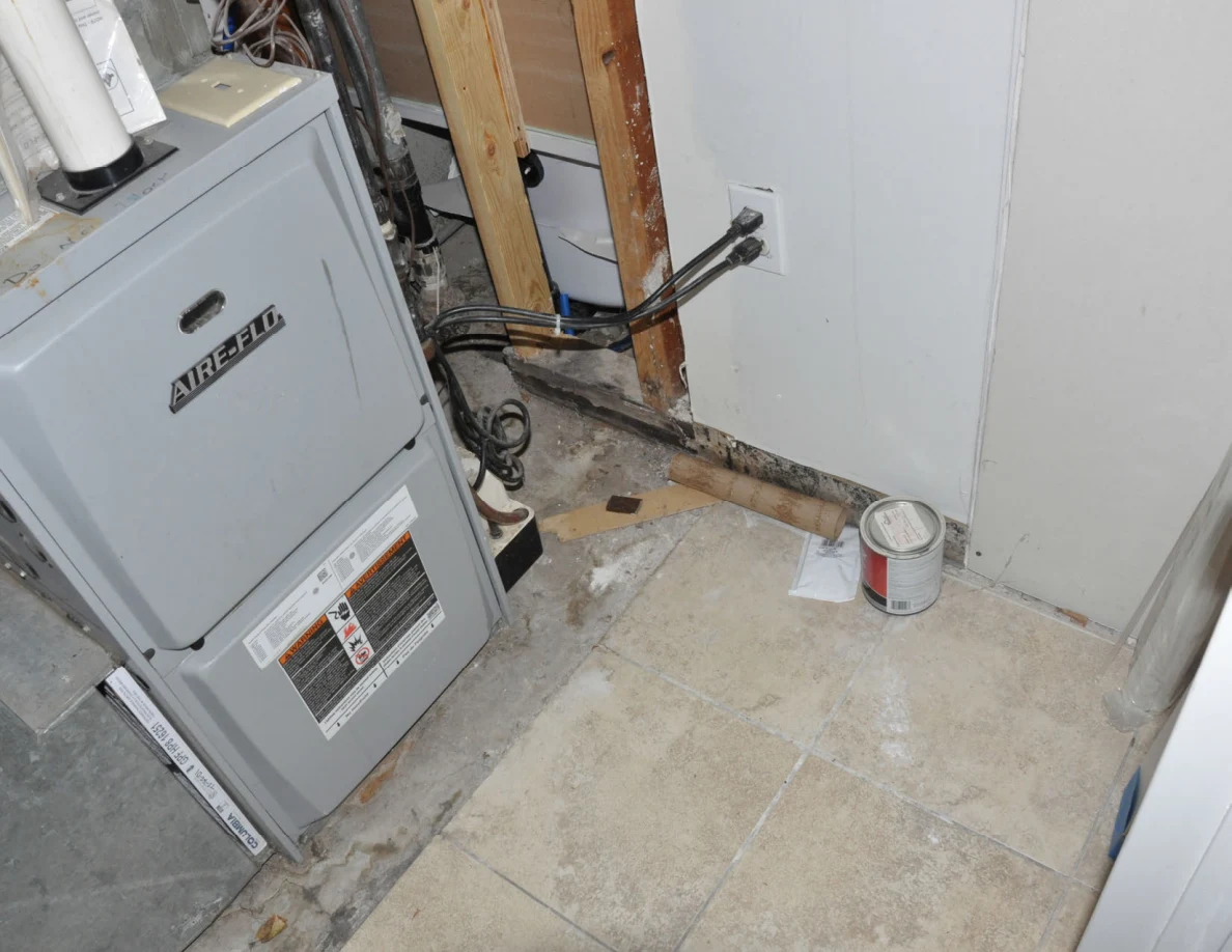 Angled view of a furnace, exposed framing, wires and a paint can on the floor.