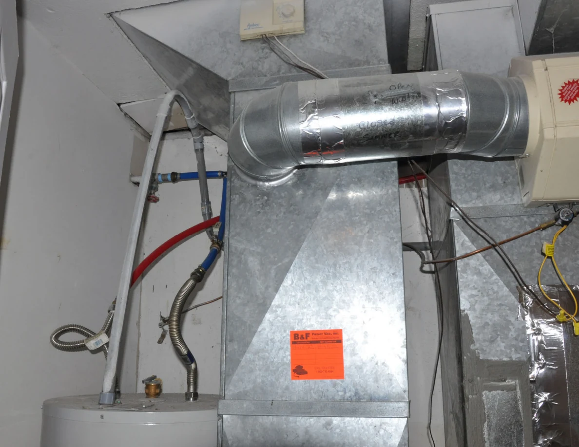Close view of metal ductwork, pipes and wires above utility equipment.