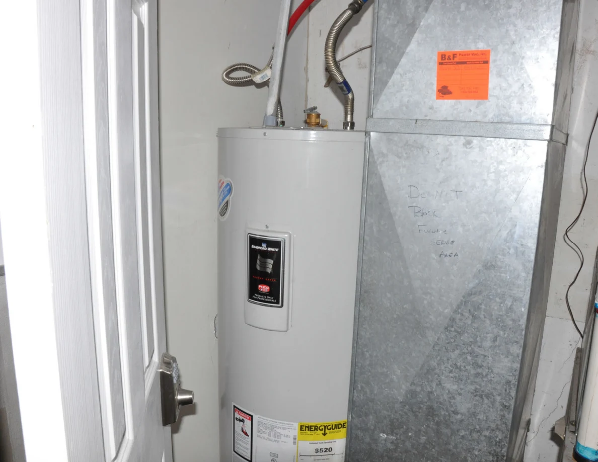 White cylindrical water heater beside galvanized ductwork and connected pipes.