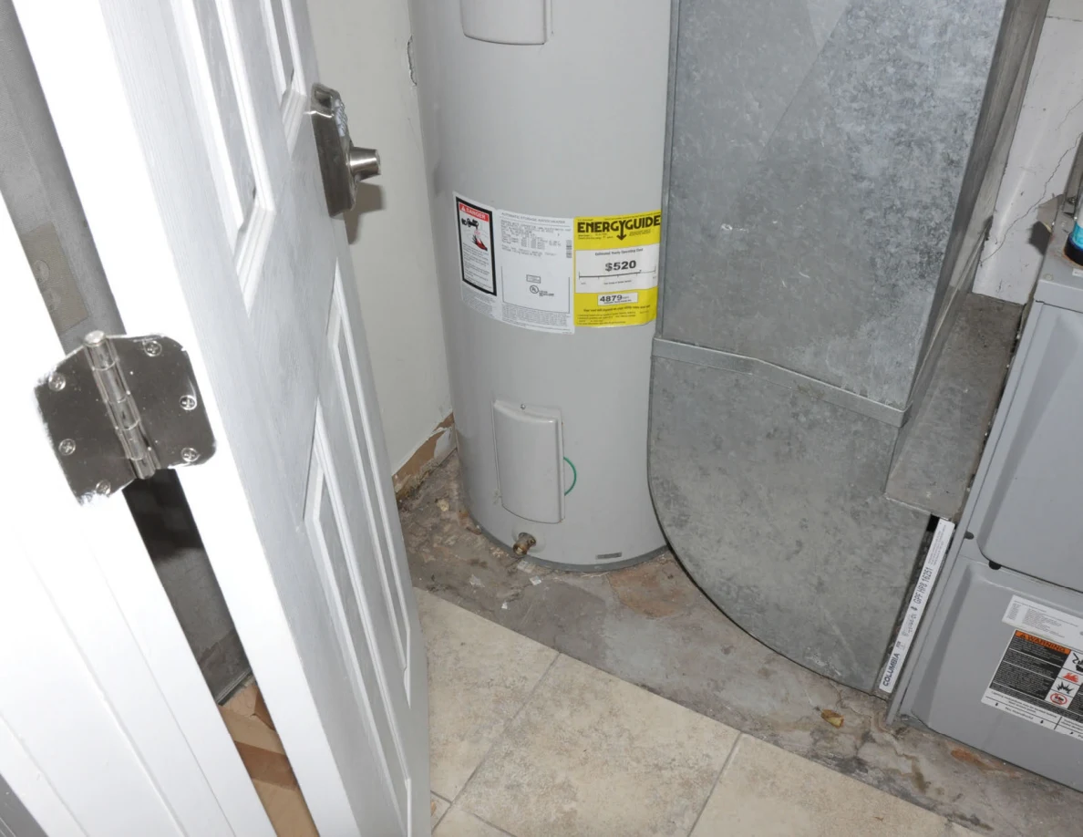 Base of a white water heater beside metal ductwork and a utility-room threshold.