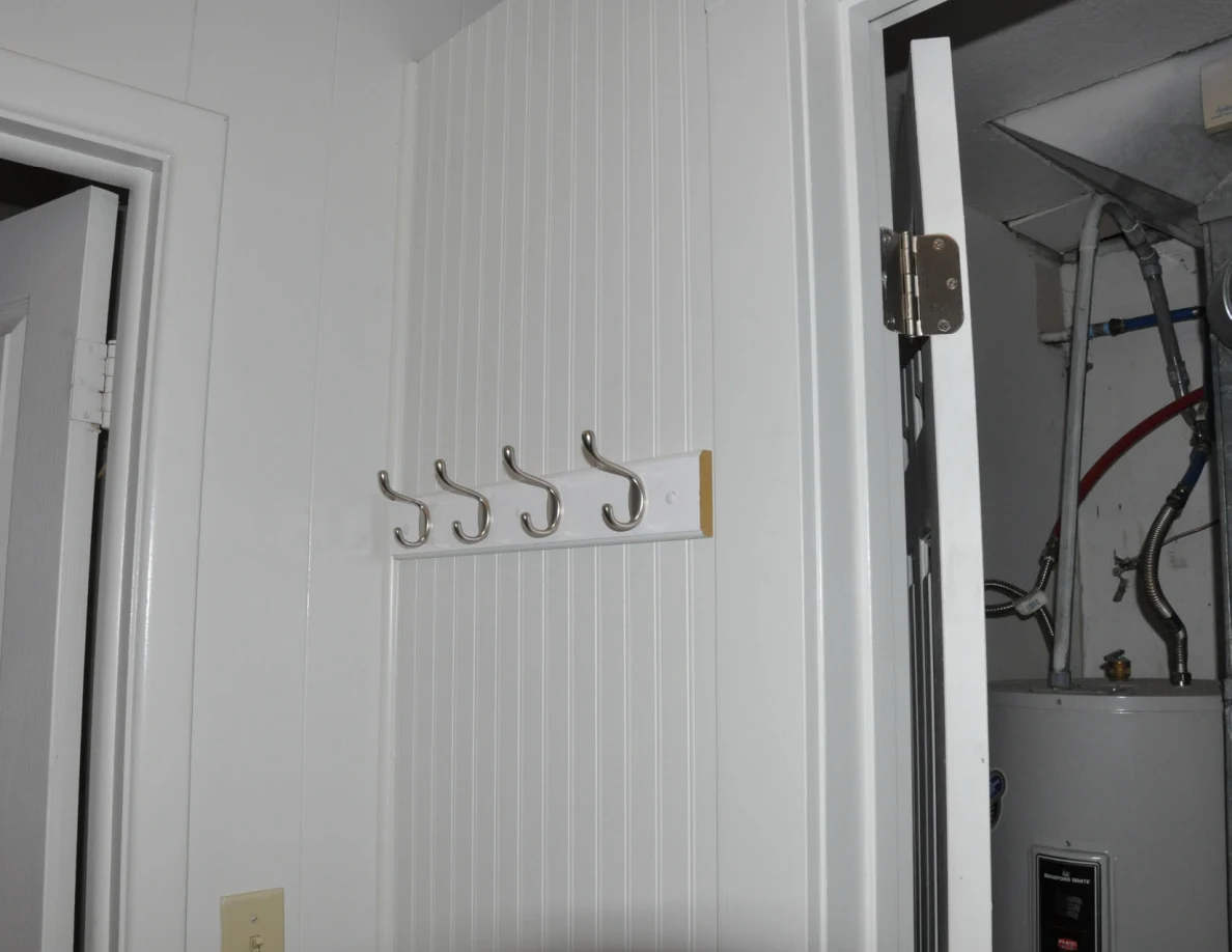Row of metal coat hooks on a paneled hallway wall beside the utility closet.