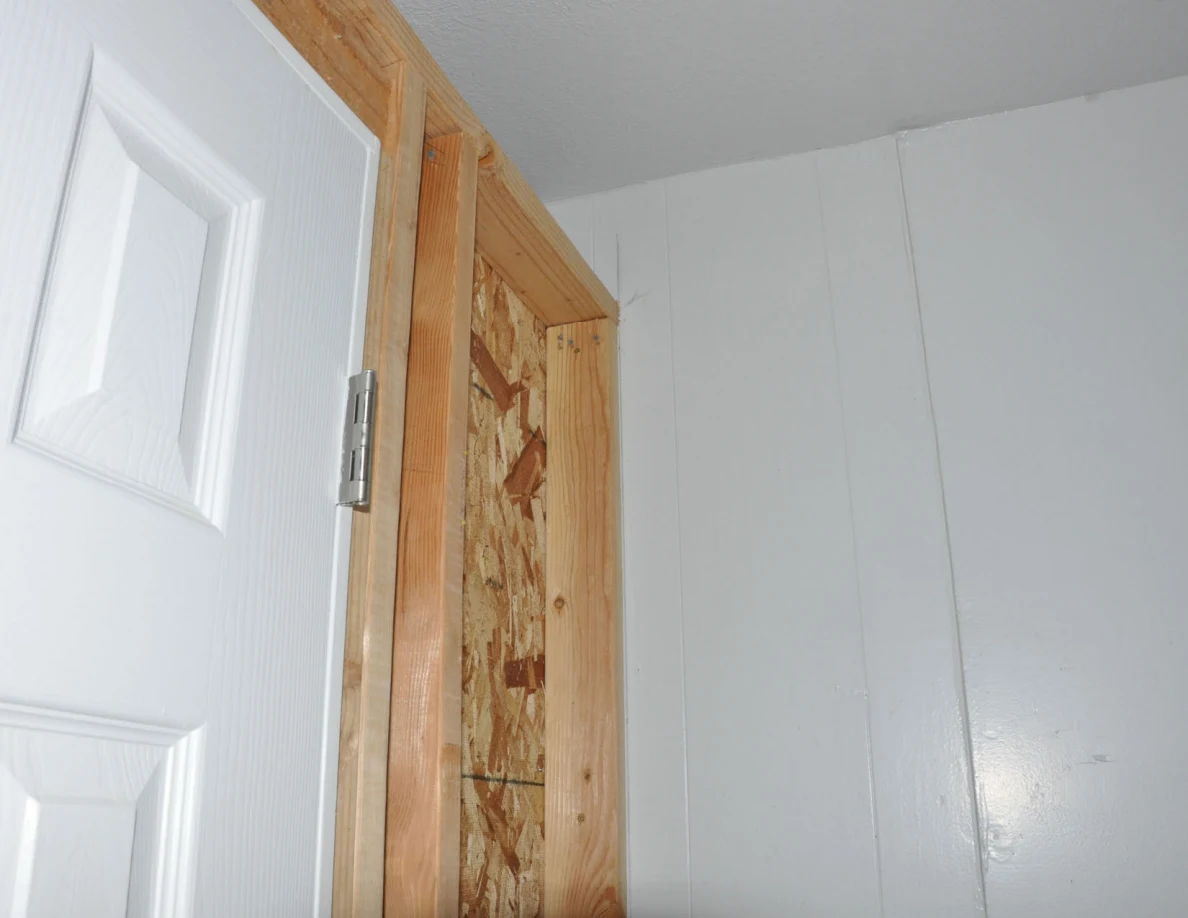 Exposed wooden door framing and particle board beside white wall panels.