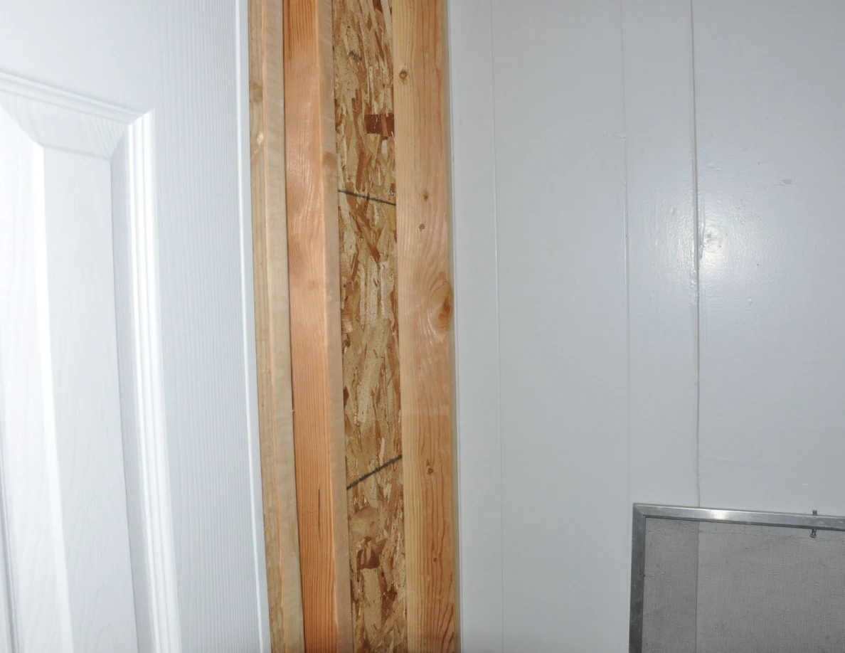Close view of exposed wood framing and particle board beside a white door.
