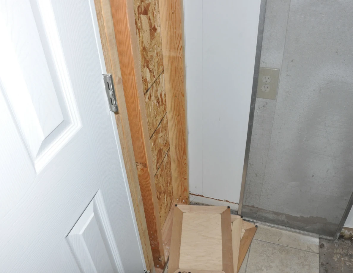 Utility-room corner with exposed framing and a loose wooden panel near the floor.