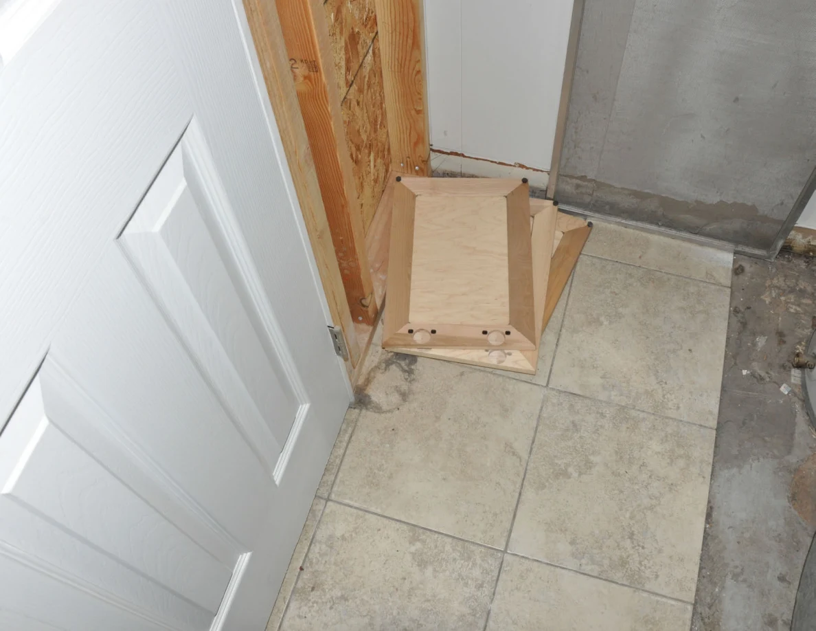Loose wooden panel lying on the tiled utility-room floor beside a metal-framed screen.
