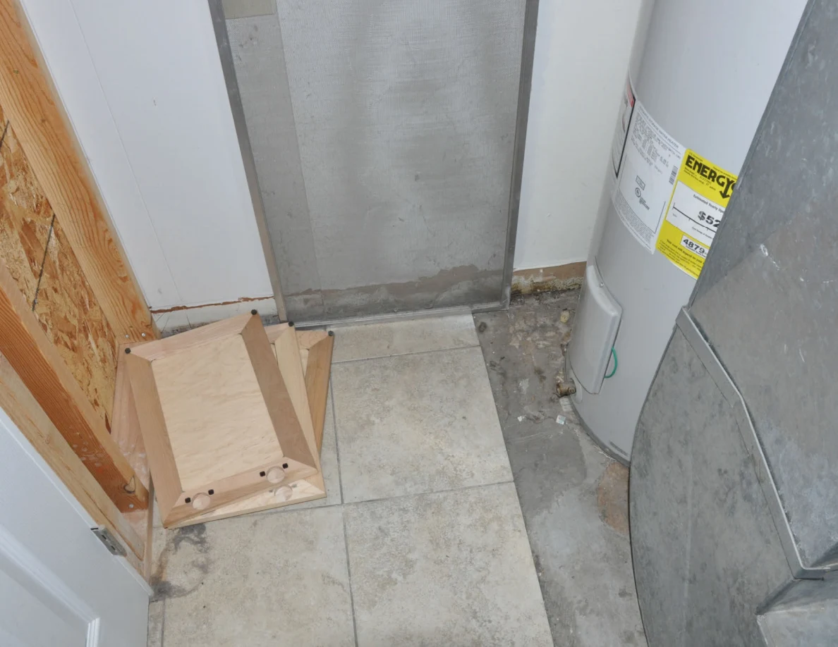 Loose wooden panel and screen beside a water heater and metal ductwork.