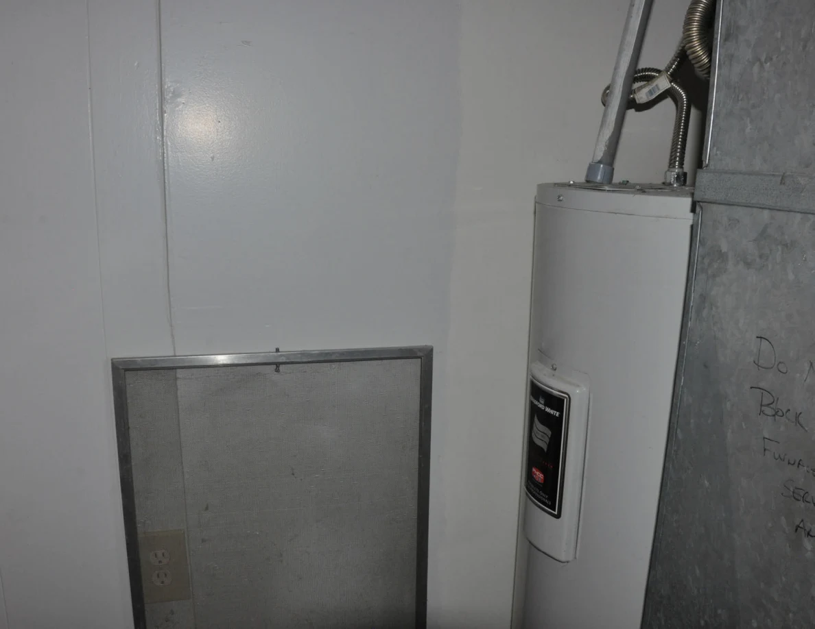 White water heater and metal duct beside a loose rectangular screen against the wall.