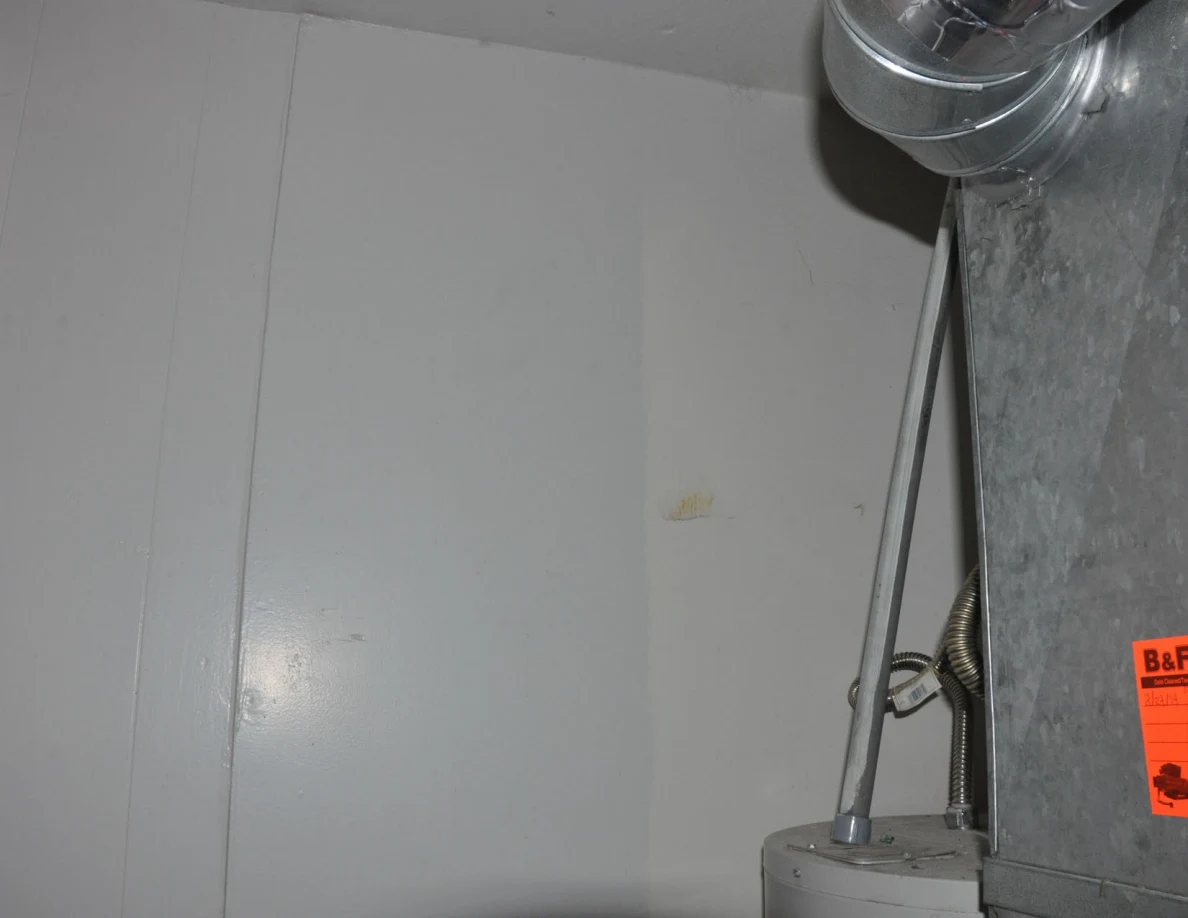 Upper white-paneled wall beside water-heater pipes and metal ductwork.
