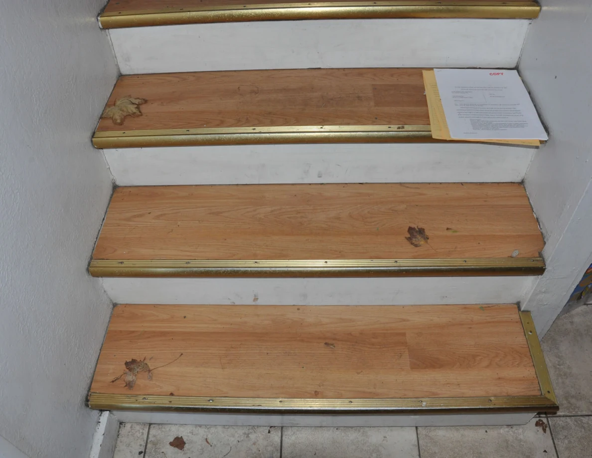 Lower wooden stairs with dry leaves and a paper resting on a tread.