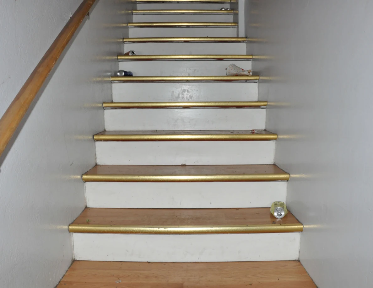 Wooden staircase with gold-colored step edges, drink cans and a paper bag.