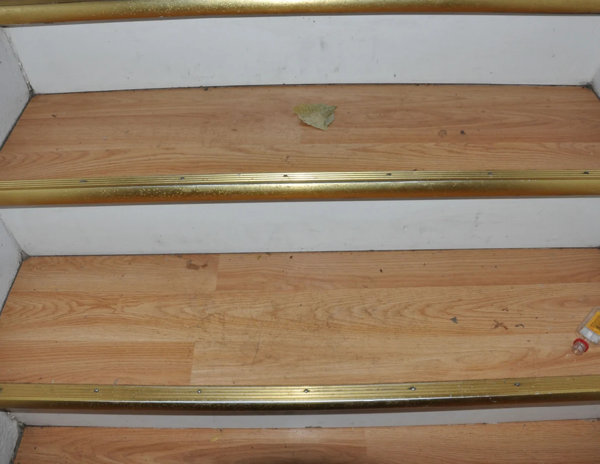 Close view of wooden stair treads with gold-colored edges and a dry leaf.