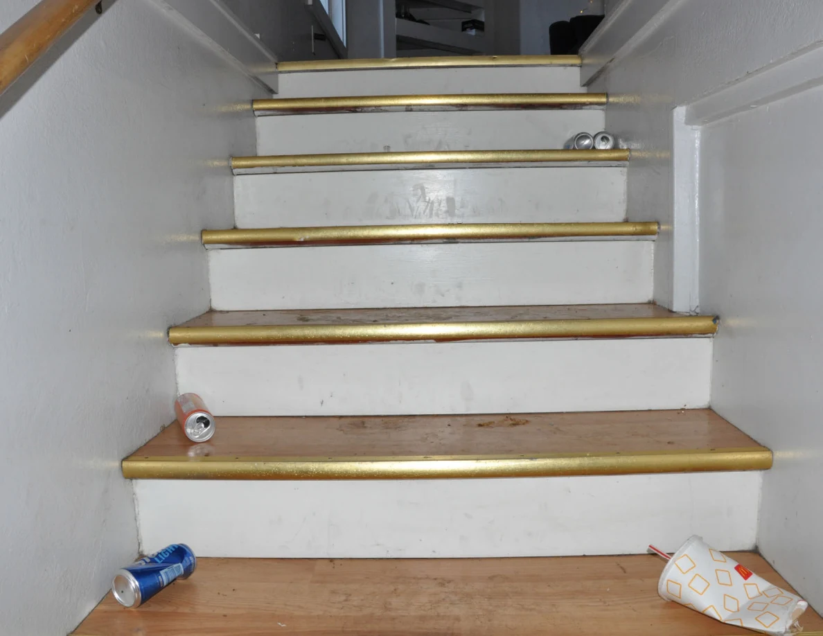 Wooden stairs with scattered drink cans and a paper bag.