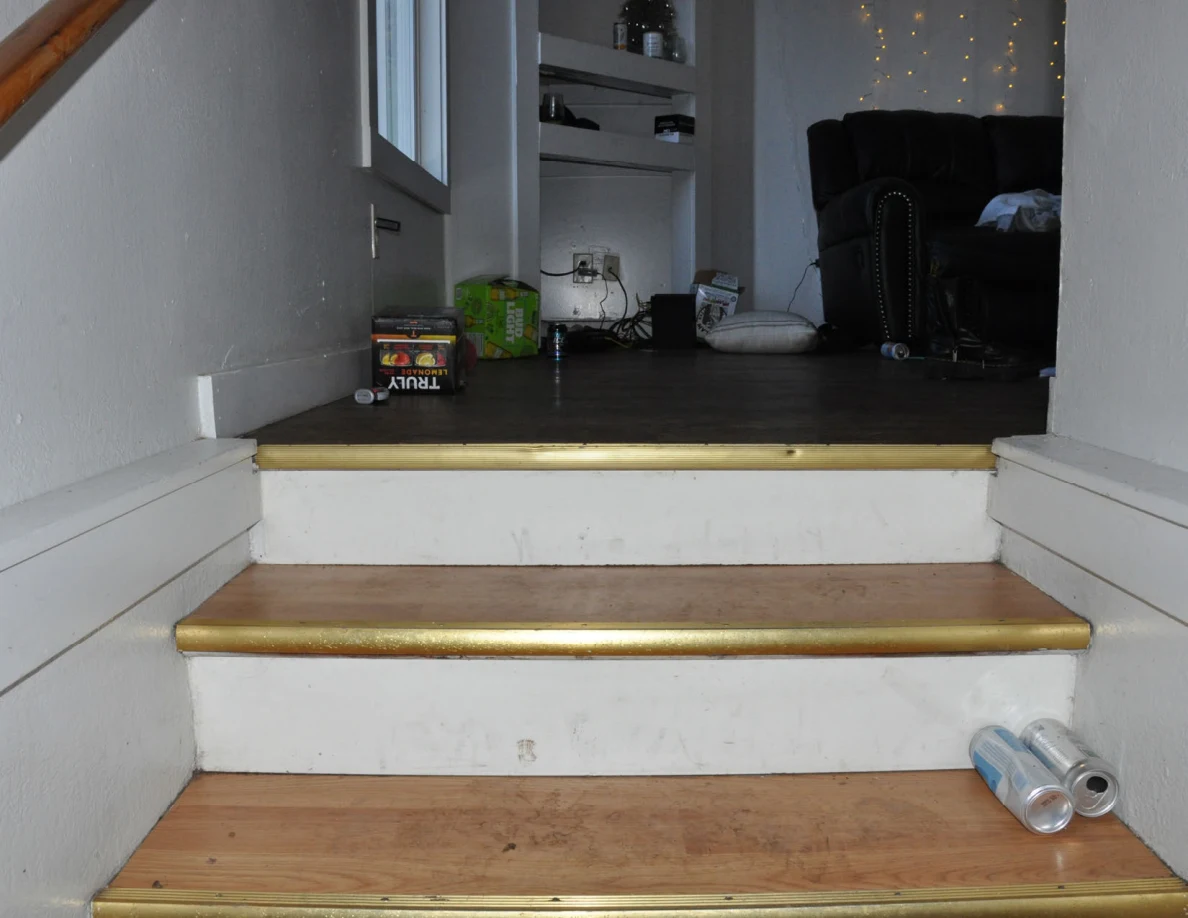 Top of stairs opening into a living room with black seating, shelves and drink containers.