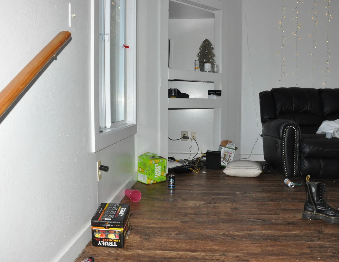 Living-room landing with drink cartons, a red cup, cables, boots and black sofa beside shelves.