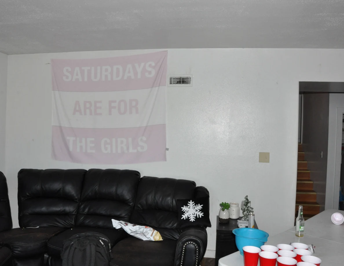 Black sofa beneath a Saturdays Are For The Girls banner, beside a folding table with red cups.