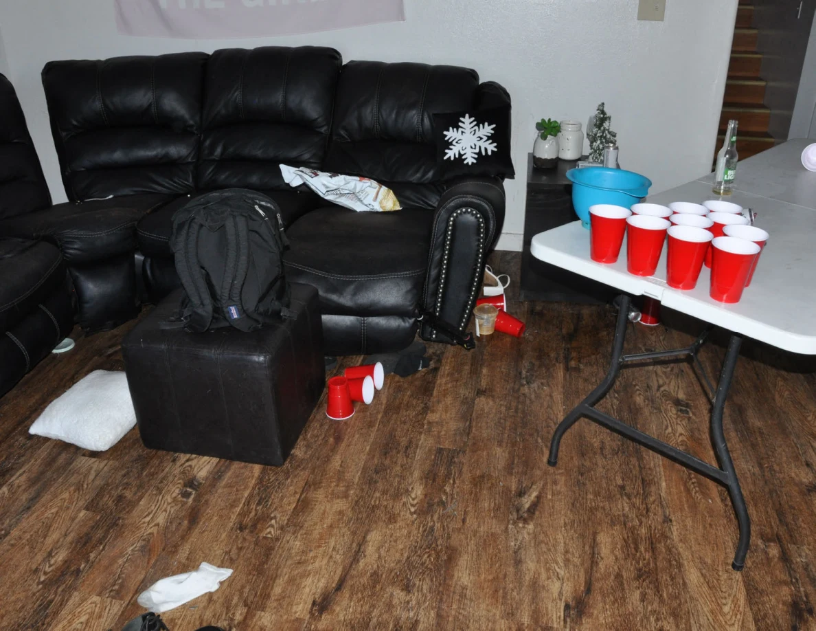 Living room with black sofa, backpack on an ottoman and a folding table arranged with red cups.