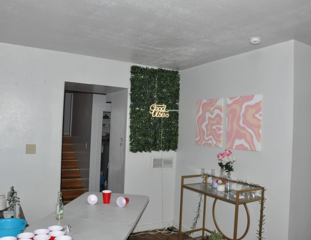 Living-room wall with illuminated Good Vibes sign, pink artwork and a gold-colored drinks cart.