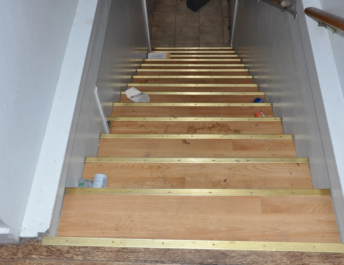Downward view of wooden stairs with gold-colored edges and scattered drink containers.