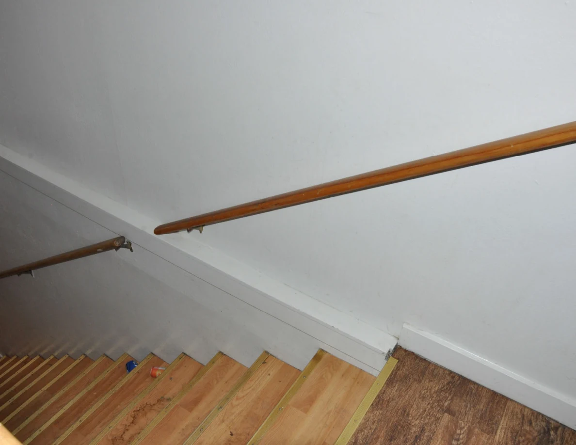 White stairwell wall with a long wooden handrail.