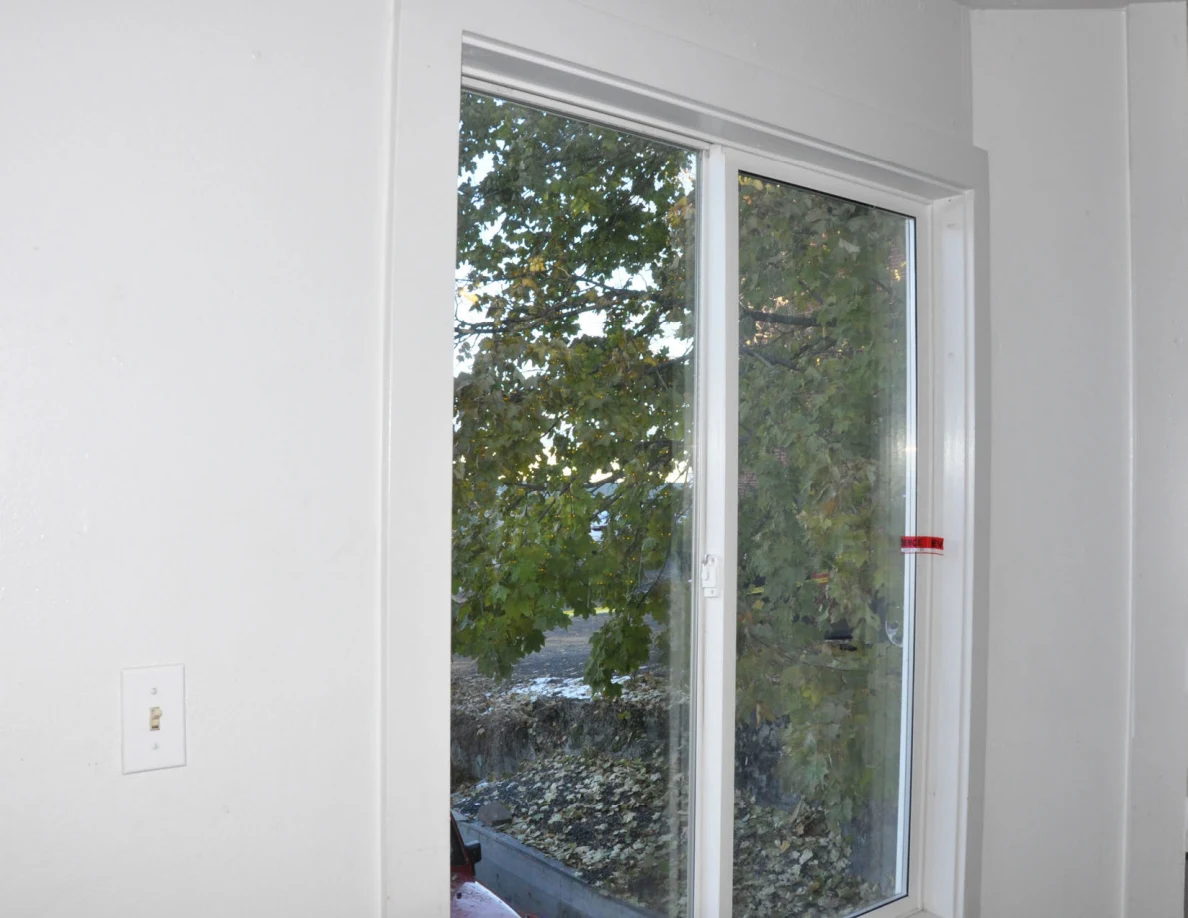 Interior window with red tape at the frame and leafy trees visible outside.
