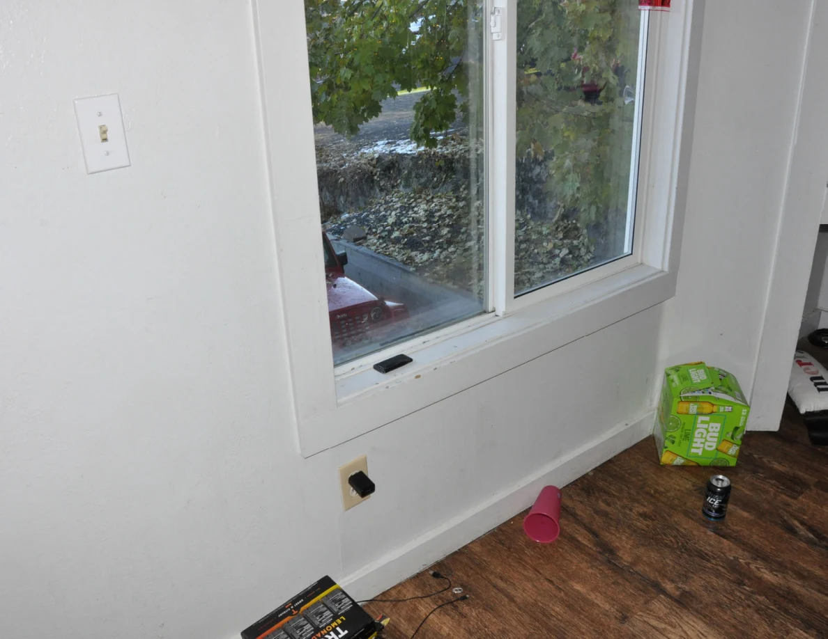 Window above a wood-look floor with a green drinks carton, can and pink cup.