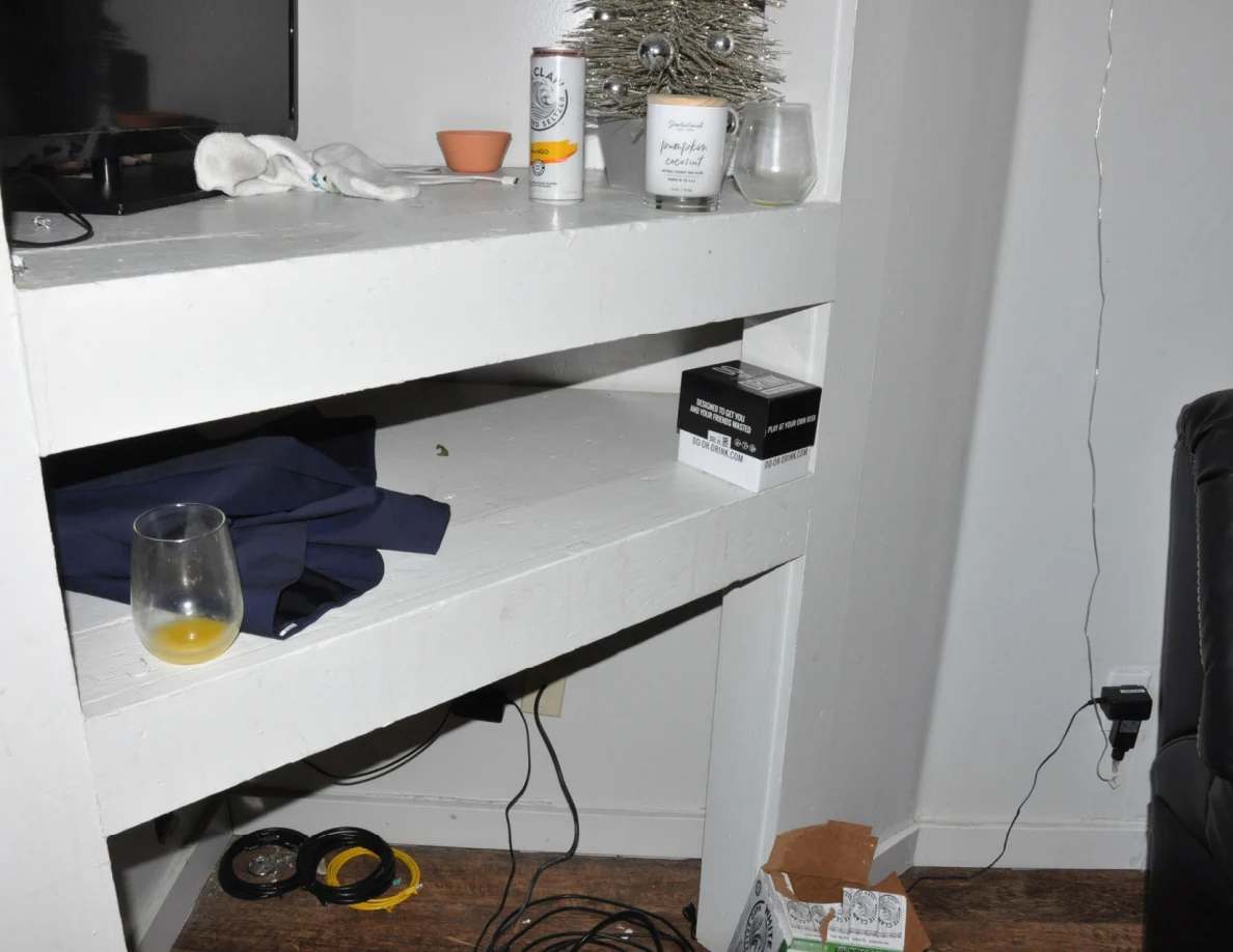 Built-in white shelves holding glassware, folded dark fabric, a small tree and containers.