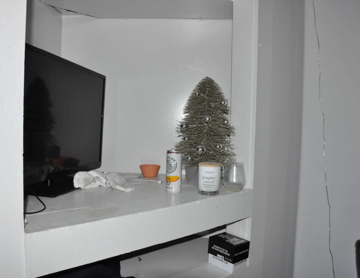 Television and small decorative tree on a white shelf with a drink can, candle and glass.