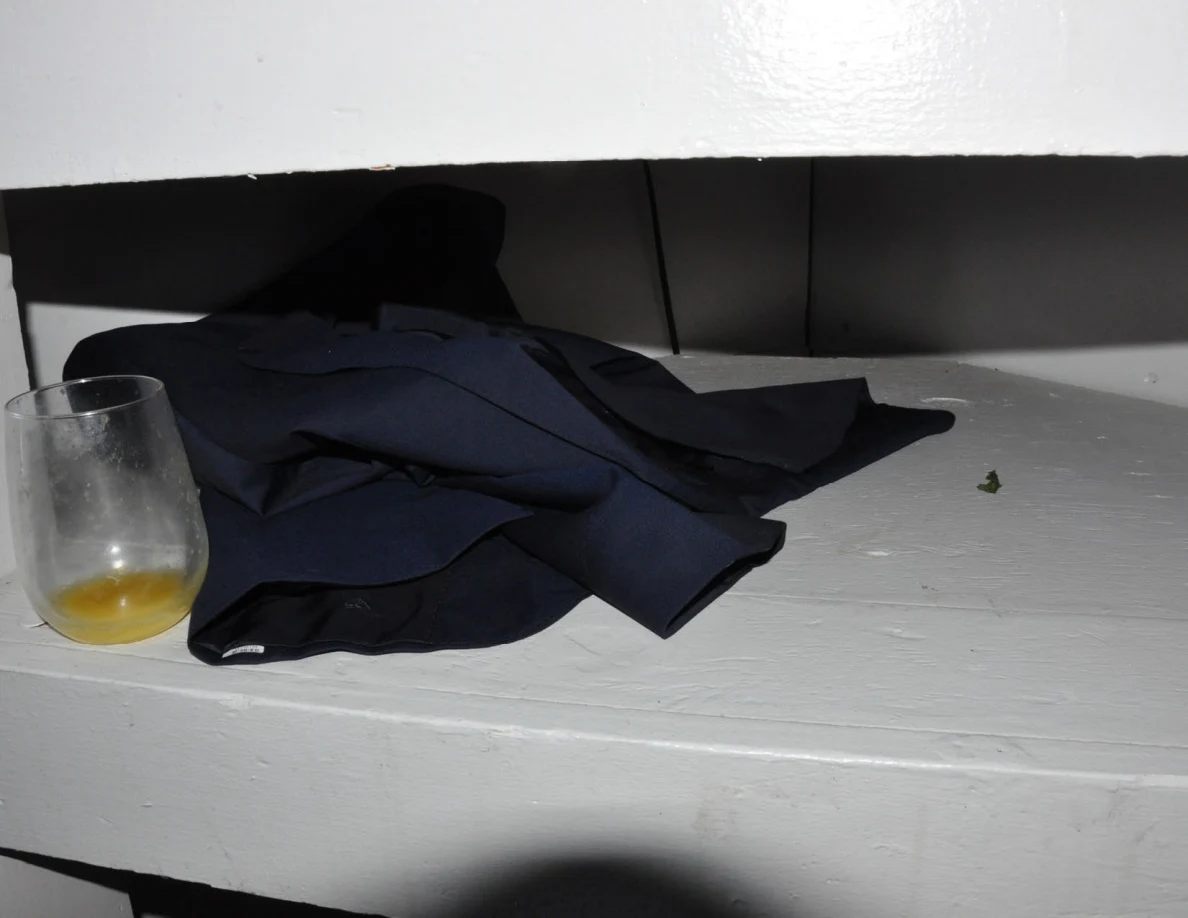 Glass containing yellow liquid beside dark folded fabric on a white shelf.