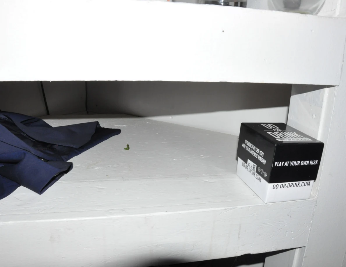 White shelf holding dark fabric and a black Do or Drink game box.
