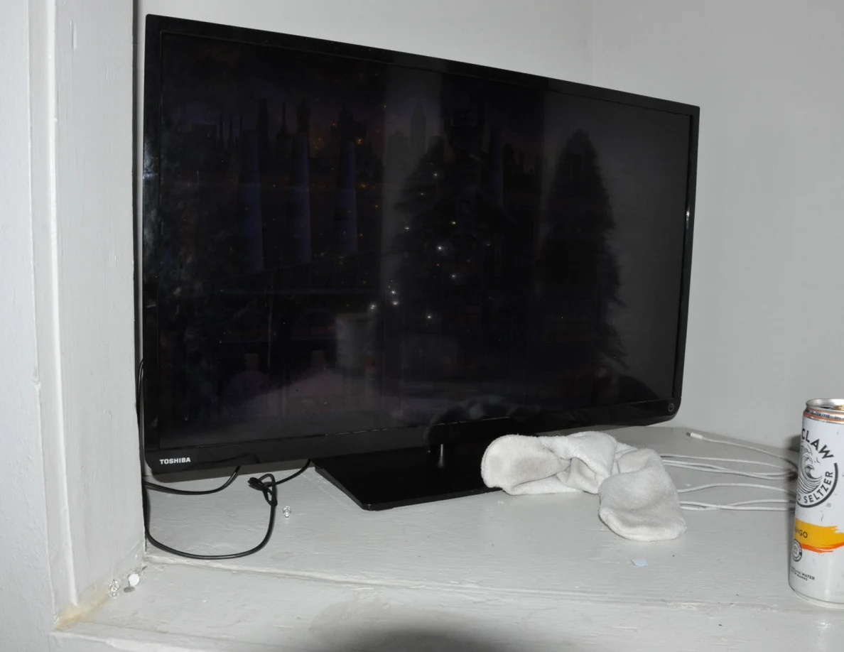 Black television on a white shelf beside a cloth and drink can.