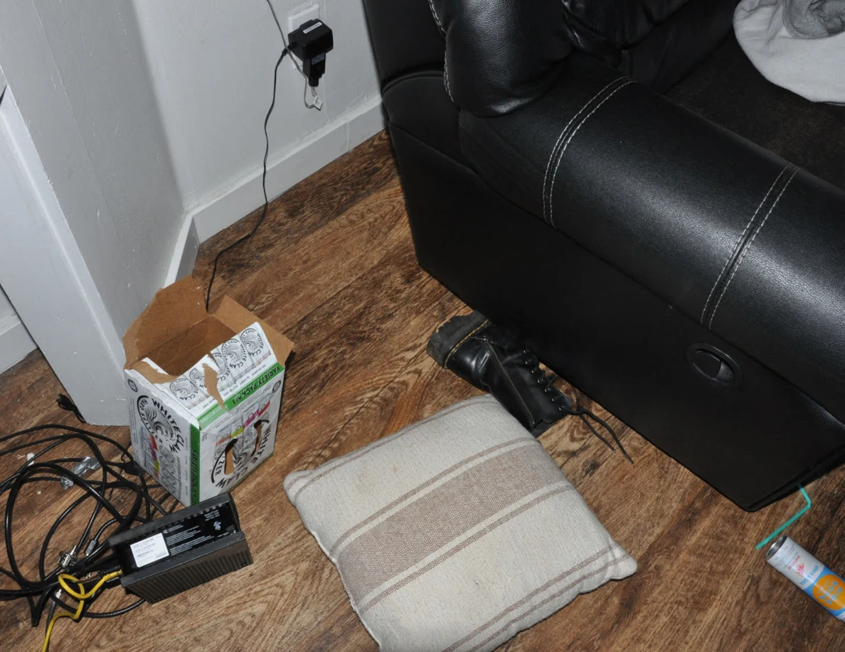 Floor beside a black sofa with cushion, drink carton, cables and a can.