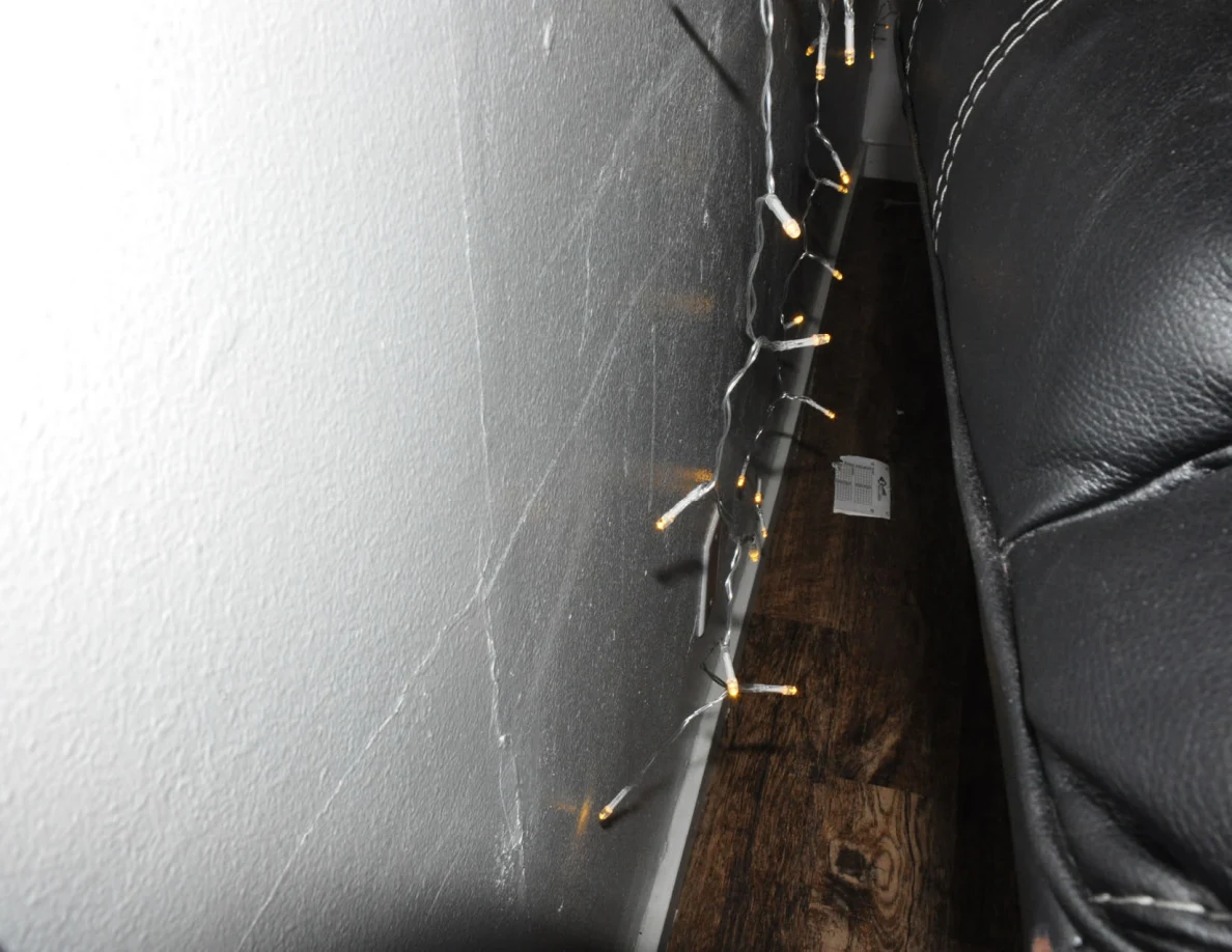 Narrow gap behind a black sofa with string lights along the wall.