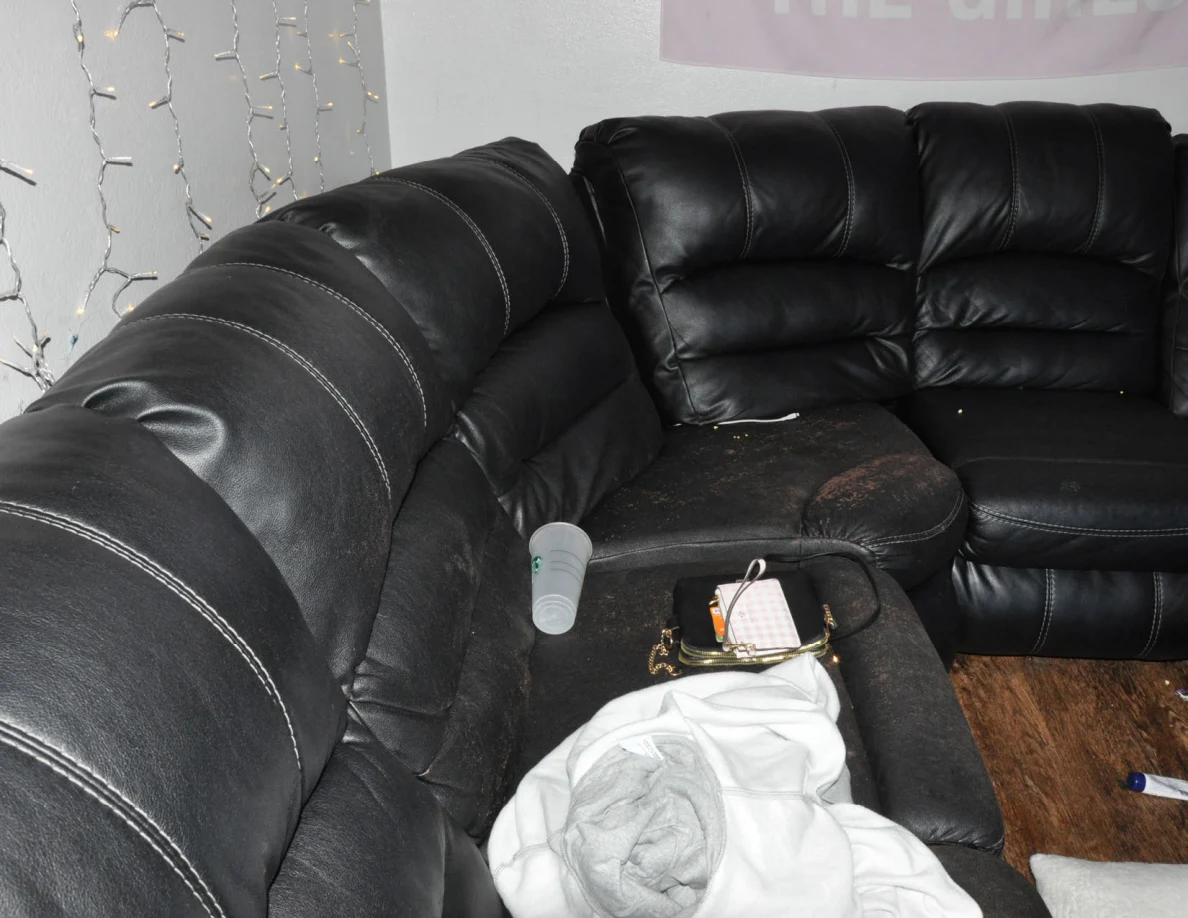 Black sectional sofa with pale fabric, a clear cup and a small purse on its cushions.