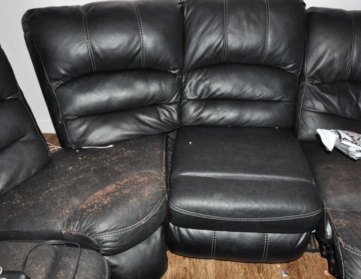 Close view of black leather sofa cushions with brown worn areas.