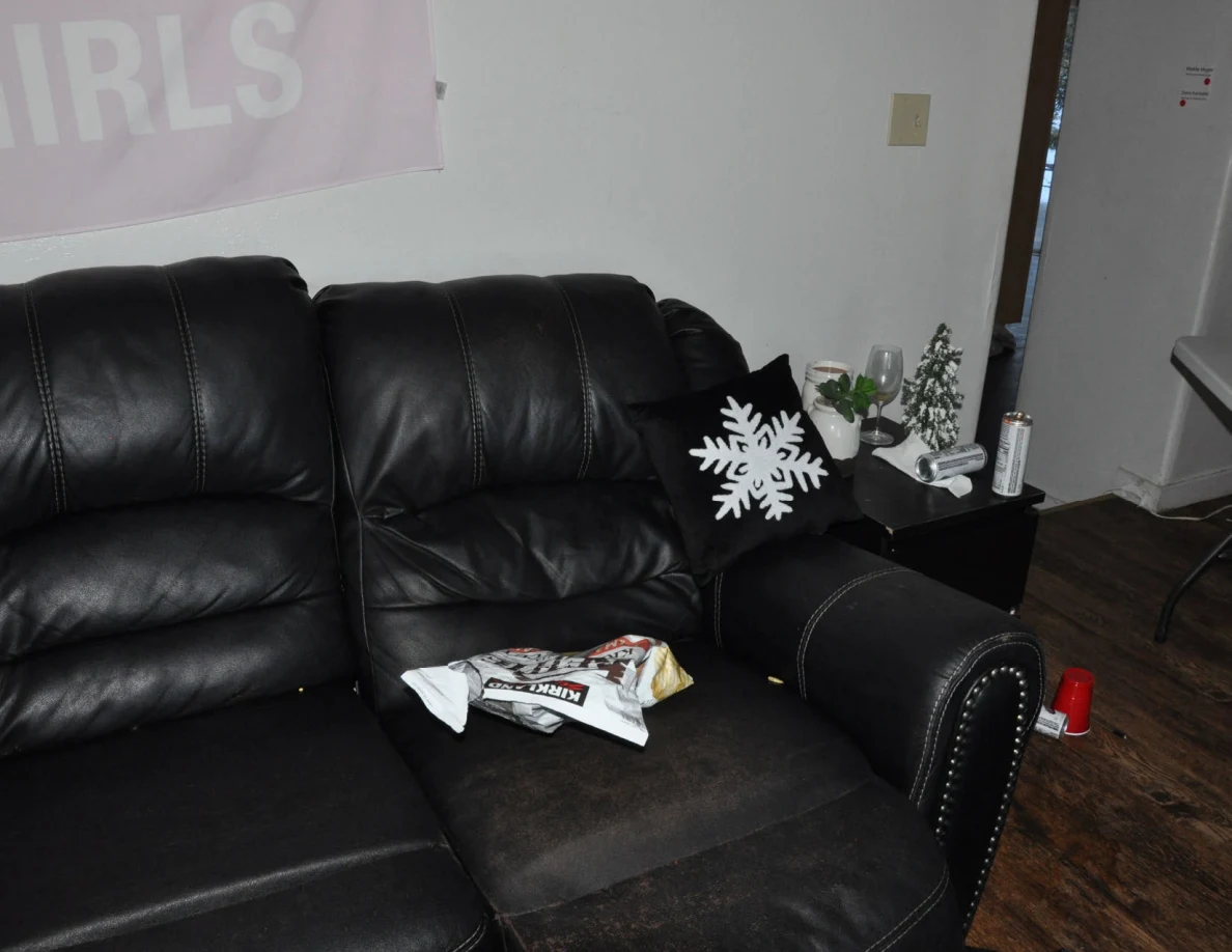 Black sofa with a snowflake pillow and crumpled packaging beside a small side table.