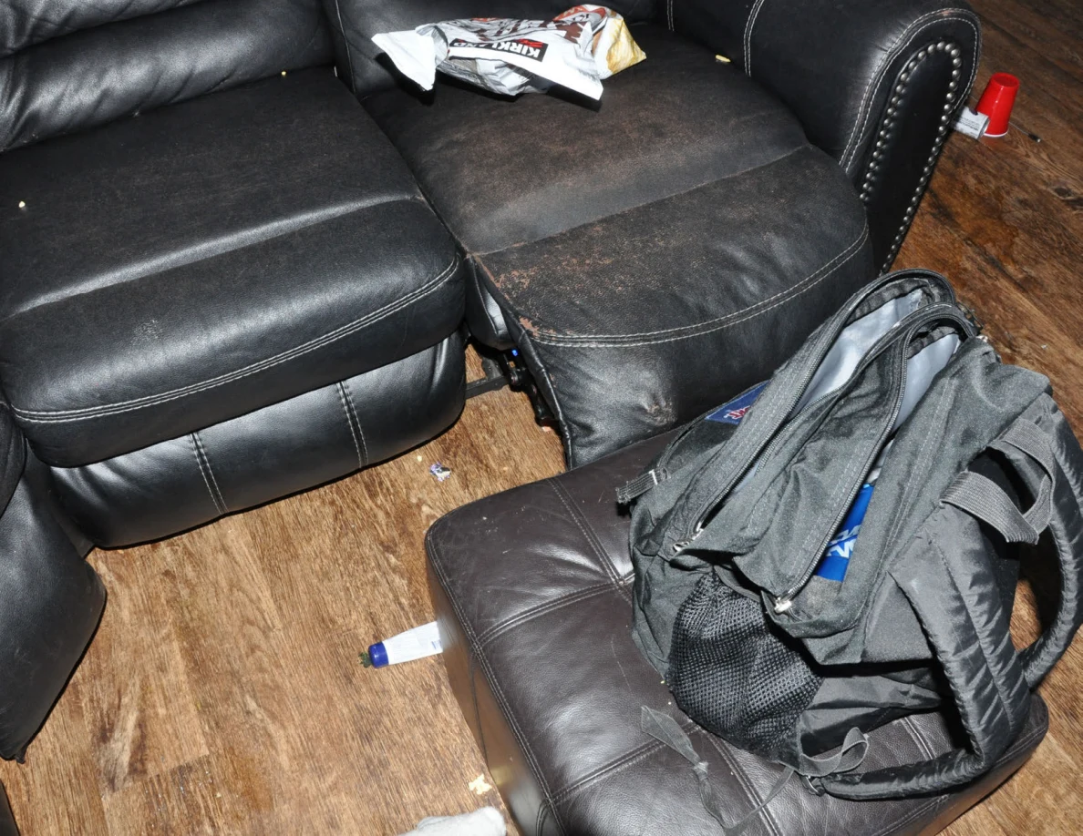 Open dark backpack on an ottoman beside worn black sofa cushions.