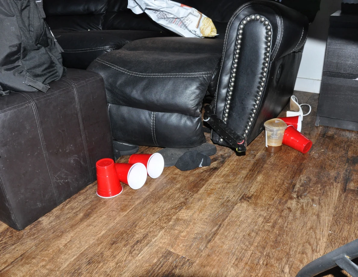 Red cups and a clear drink cup on the floor beside a black sofa and ottoman.