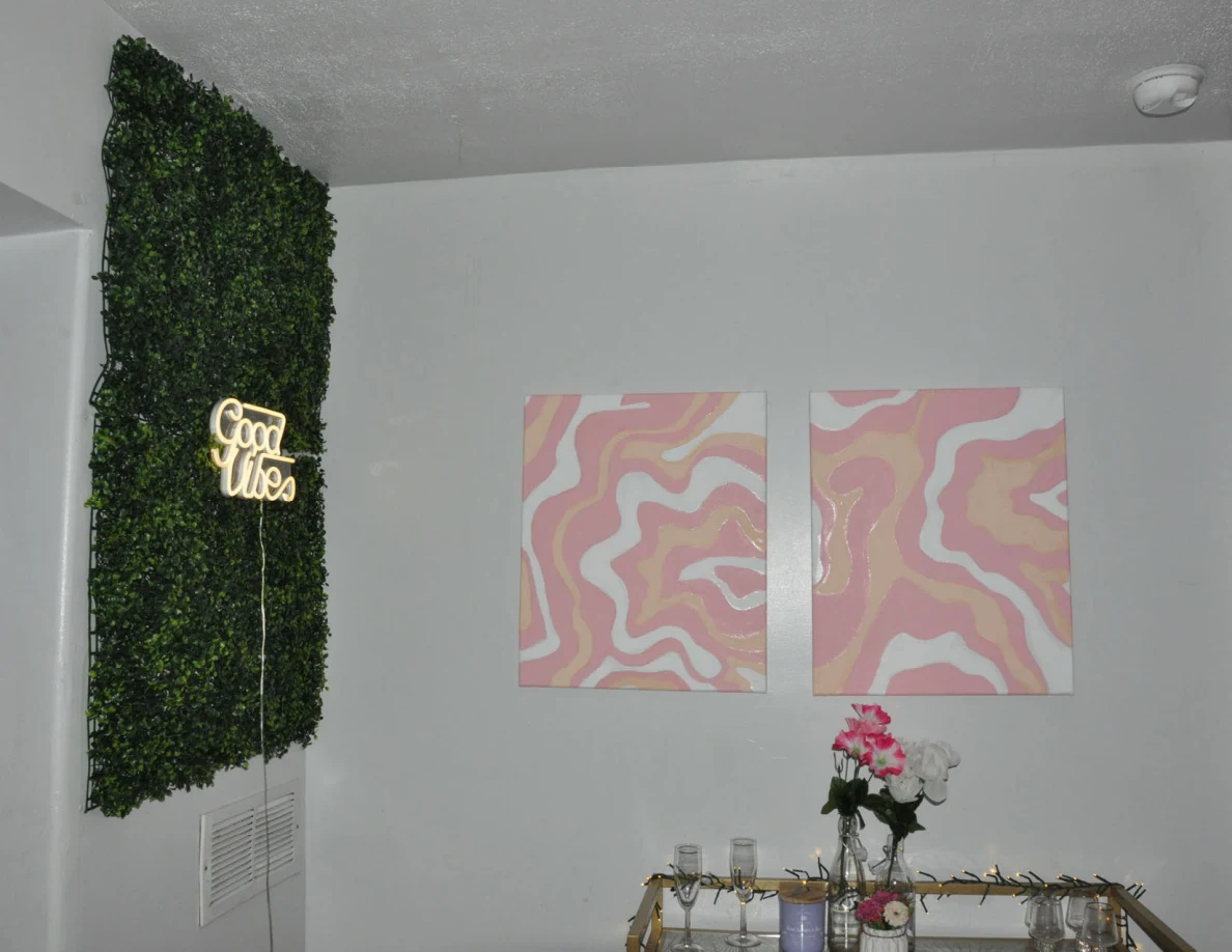 Green wall panel with illuminated Good Vibes sign beside two pink abstract pictures.
