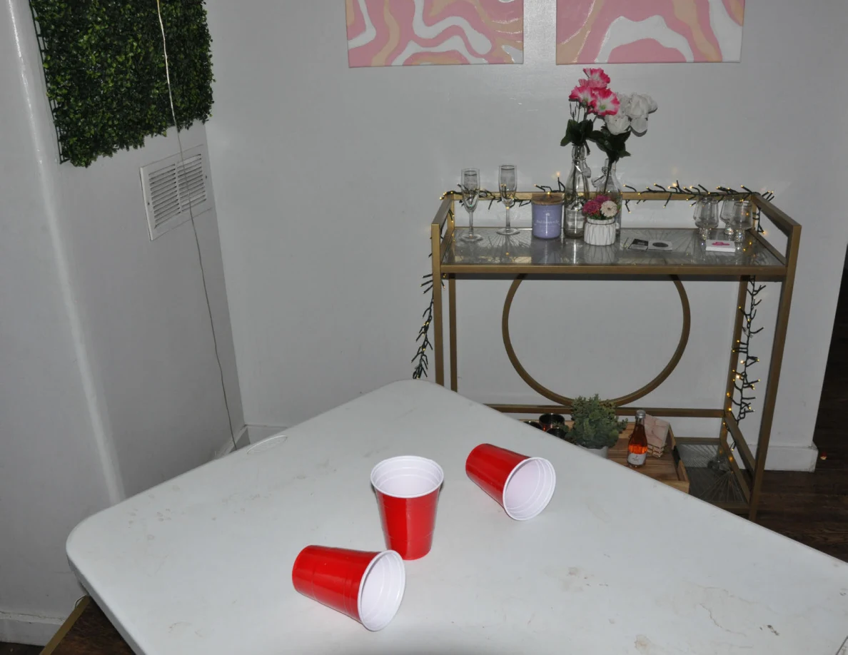 End of a folding table with red cups beside a gold-colored drinks cart and flowers.